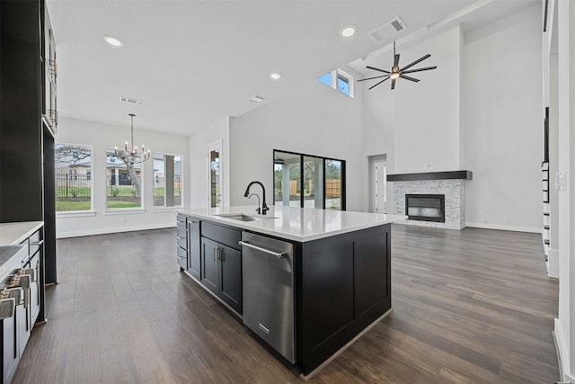 kitchen with a stone fireplace, sink, hanging light fixtures, stainless steel dishwasher, and a kitchen island with sink