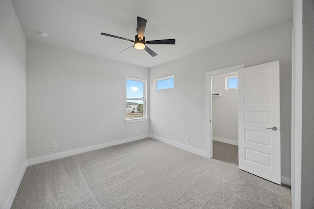 unfurnished bedroom featuring a walk in closet, light colored carpet, ceiling fan, and a closet