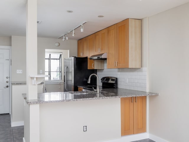 kitchen with light stone countertops, tasteful backsplash, kitchen peninsula, dark tile patterned flooring, and appliances with stainless steel finishes