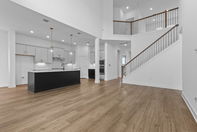 kitchen with white cabinetry, light hardwood / wood-style floors, pendant lighting, and an island with sink