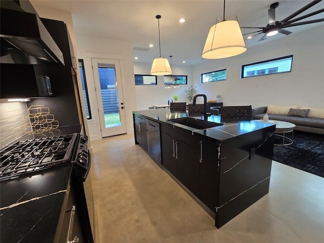 kitchen featuring range with gas cooktop, pendant lighting, wall chimney exhaust hood, a kitchen island with sink, and sink