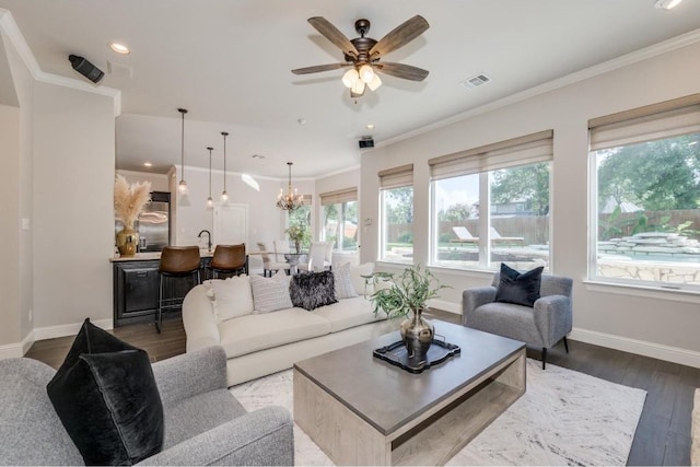 living room with wood-type flooring, ceiling fan with notable chandelier, ornamental molding, and sink