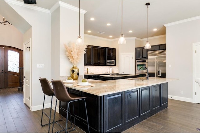 kitchen with appliances with stainless steel finishes, a kitchen breakfast bar, light stone counters, sink, and pendant lighting