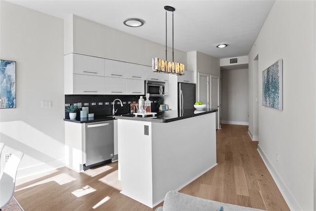 kitchen featuring white cabinets, hanging light fixtures, backsplash, light hardwood / wood-style flooring, and stainless steel appliances