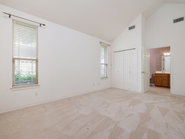 unfurnished bedroom featuring ensuite bath, high vaulted ceiling, a closet, and light colored carpet