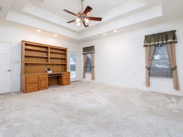 unfurnished living room with light colored carpet, ceiling fan, a tray ceiling, and crown molding