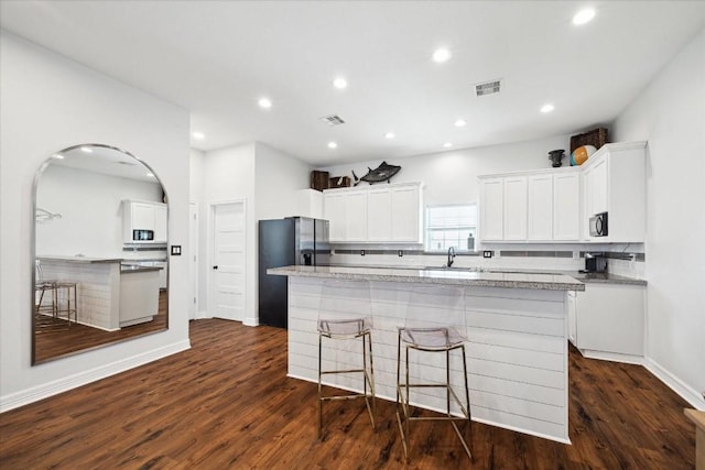 kitchen featuring dark hardwood / wood-style flooring, tasteful backsplash, white cabinetry, and an island with sink