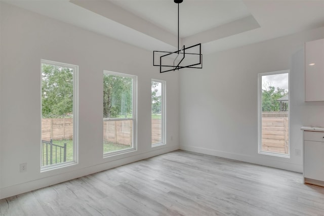 unfurnished dining area with light hardwood / wood-style flooring, a raised ceiling, and a notable chandelier