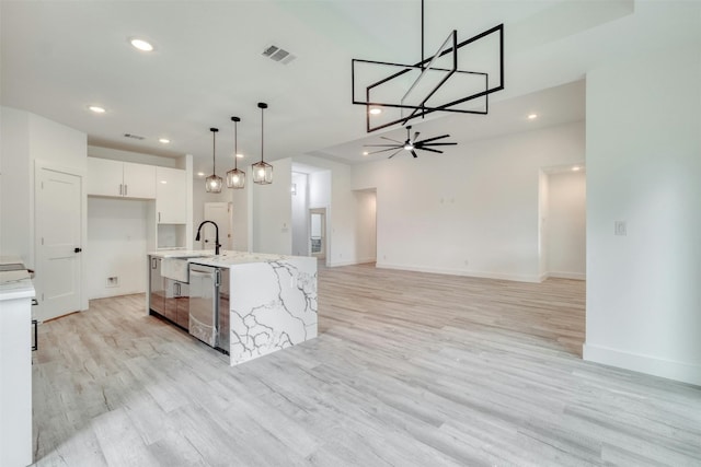 kitchen with stainless steel dishwasher, pendant lighting, white cabinets, light hardwood / wood-style floors, and an island with sink