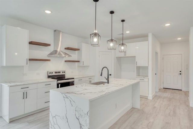 kitchen with stainless steel electric range oven, sink, wall chimney range hood, a center island with sink, and white cabinetry