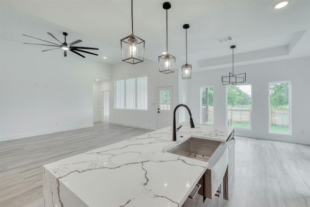 kitchen with pendant lighting, light stone counters, and an island with sink