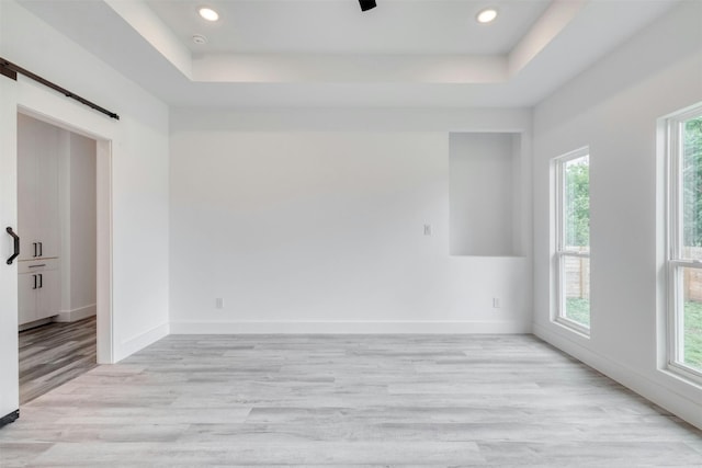 empty room with a tray ceiling, a barn door, and light hardwood / wood-style flooring