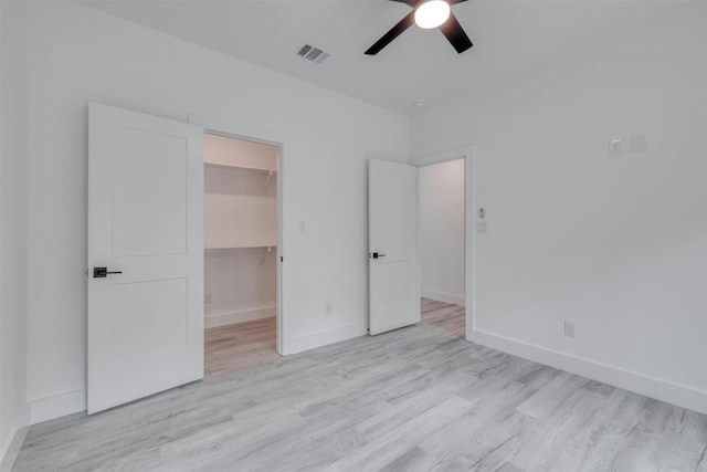 unfurnished bedroom with ceiling fan, light hardwood / wood-style floors, a walk in closet, and a closet