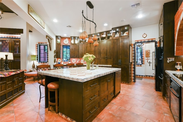 kitchen with a center island, a kitchen breakfast bar, decorative light fixtures, black oven, and sink