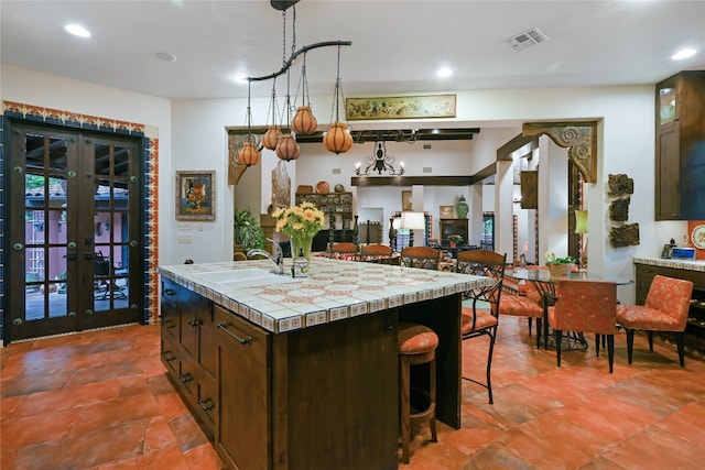 kitchen with a center island with sink, tile flooring, tile countertops, sink, and french doors