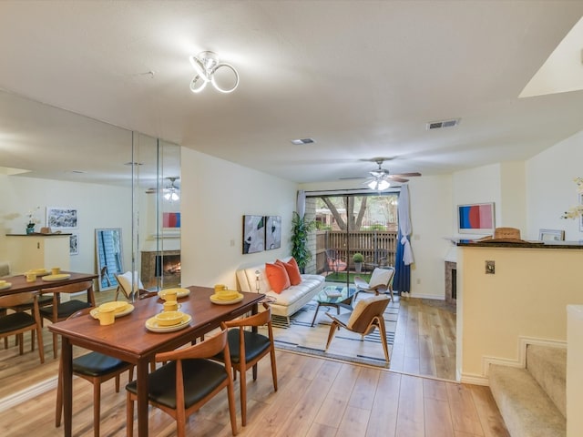 dining area featuring light wood-style flooring, visible vents, a lit fireplace, and a ceiling fan