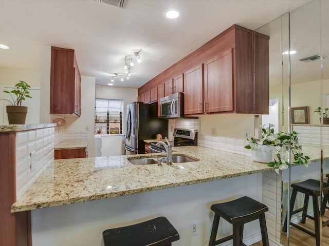 kitchen with appliances with stainless steel finishes, kitchen peninsula, light stone countertops, wood-type flooring, and sink