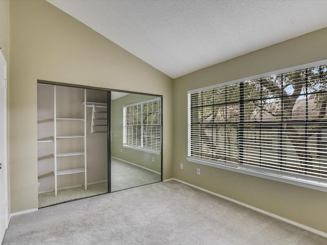 unfurnished bedroom with baseboards, lofted ceiling, carpet flooring, a closet, and a textured ceiling