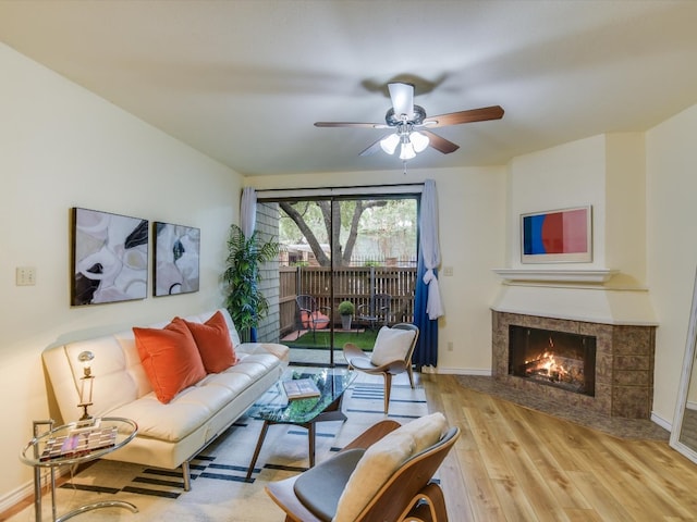 living area with light wood-type flooring, ceiling fan, baseboards, and a tiled fireplace