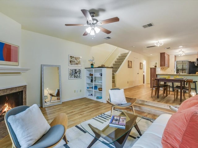 living room with stairway, light wood-style flooring, visible vents, and a lit fireplace