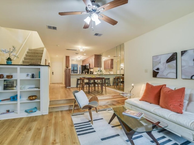 living room with stairway, a ceiling fan, visible vents, and light wood finished floors