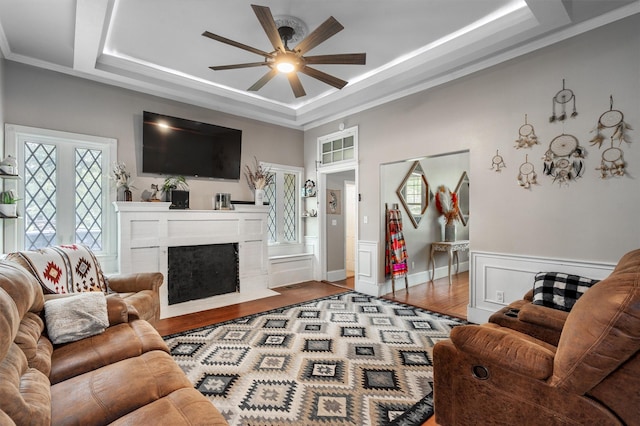 living room with hardwood / wood-style floors, a fireplace, ornamental molding, ceiling fan, and a tray ceiling