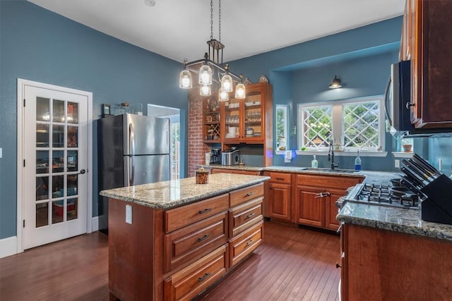 kitchen with sink, a center island, dark hardwood / wood-style flooring, pendant lighting, and light stone countertops