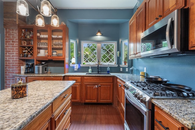 kitchen with sink, dark wood-type flooring, appliances with stainless steel finishes, hanging light fixtures, and light stone counters