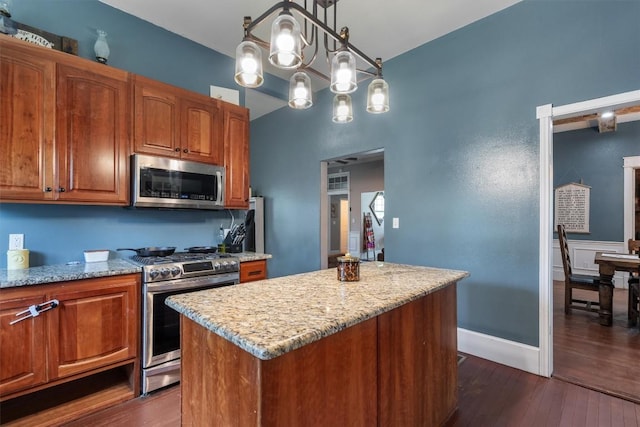 kitchen with light stone counters, hanging light fixtures, appliances with stainless steel finishes, dark hardwood / wood-style floors, and a kitchen island