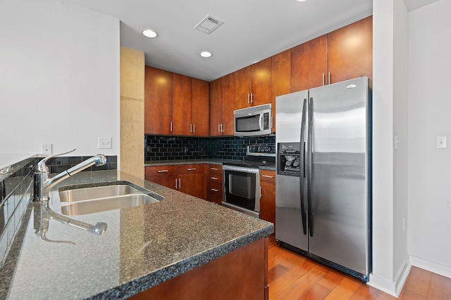 kitchen with tasteful backsplash, stainless steel appliances, sink, light hardwood / wood-style flooring, and dark stone countertops