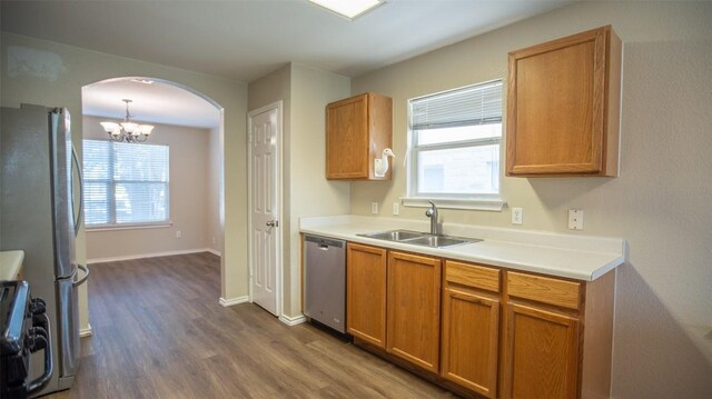 kitchen with appliances with stainless steel finishes, sink, pendant lighting, hardwood / wood-style flooring, and a notable chandelier