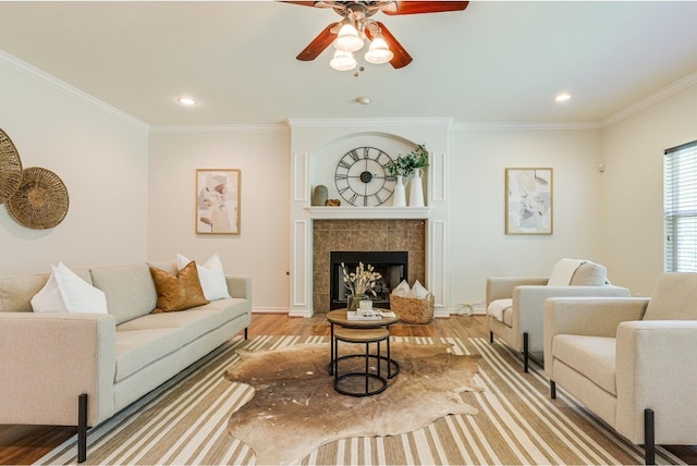 living room featuring a tile fireplace, ornamental molding, ceiling fan, and light hardwood / wood-style floors