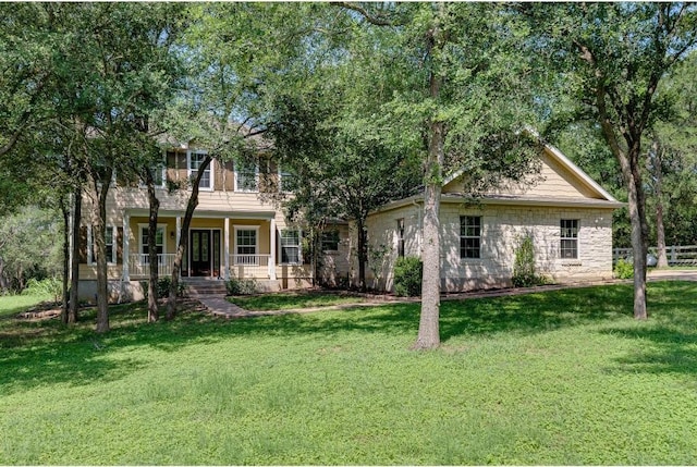 view of property hidden behind natural elements with stone siding, covered porch, a balcony, and a front lawn