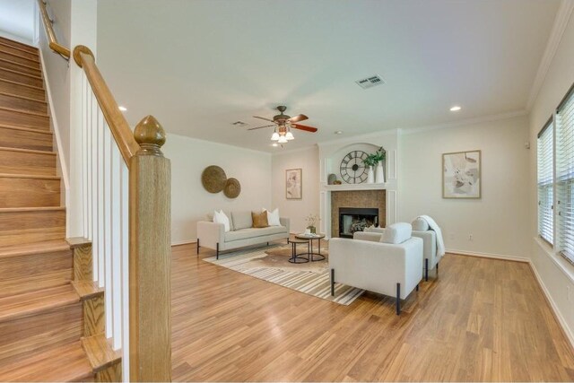 living room with a tile fireplace, crown molding, light wood-type flooring, and ceiling fan