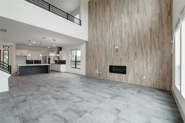 unfurnished living room with visible vents, stairs, a towering ceiling, heating unit, and a glass covered fireplace