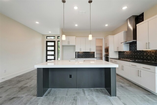 kitchen with backsplash, an island with sink, stainless steel appliances, wall chimney exhaust hood, and a sink