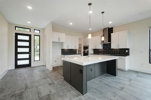 kitchen with stainless steel appliances, a sink, white cabinets, pendant lighting, and wall chimney exhaust hood