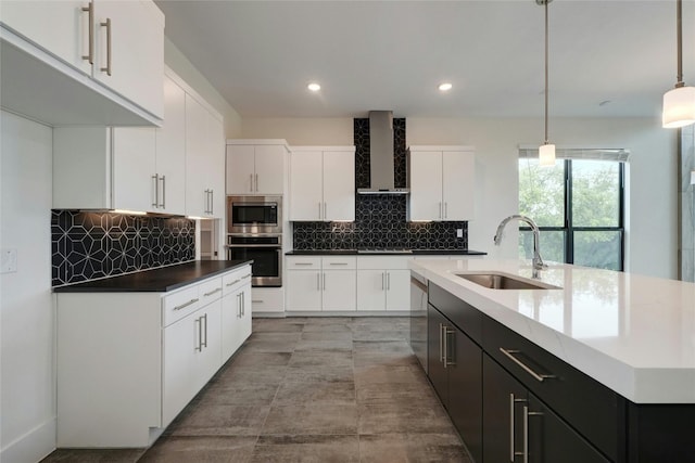 kitchen with pendant lighting, a sink, appliances with stainless steel finishes, wall chimney exhaust hood, and white cabinets