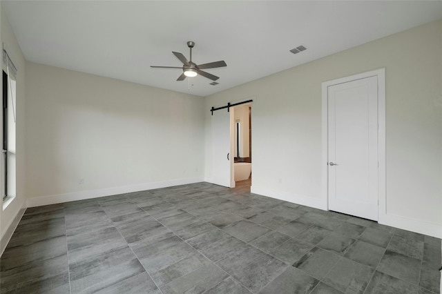 unfurnished bedroom with baseboards, visible vents, ensuite bath, ceiling fan, and a barn door