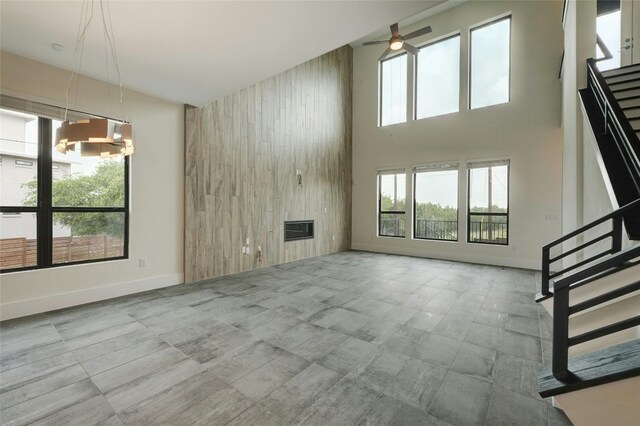 unfurnished living room featuring baseboards, a high ceiling, stairs, wood walls, and ceiling fan with notable chandelier