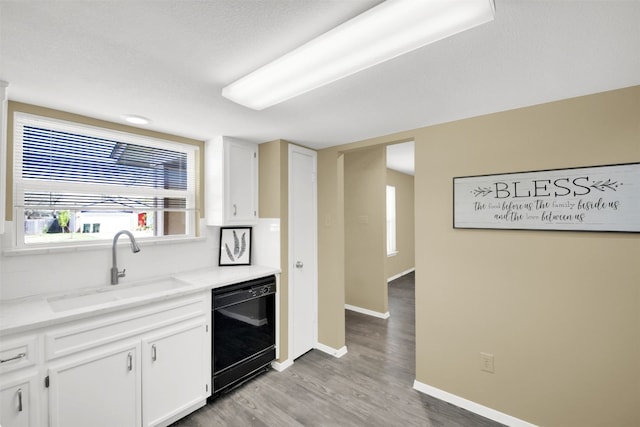 kitchen featuring dishwasher, a sink, light wood-style flooring, white cabinetry, and baseboards