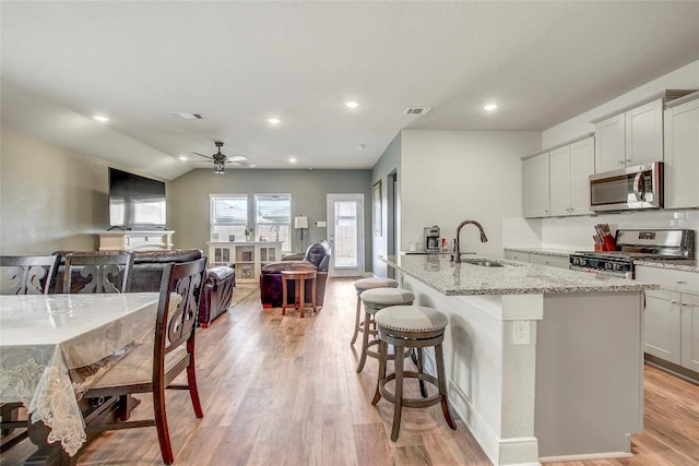 kitchen with light stone countertops, appliances with stainless steel finishes, a kitchen breakfast bar, sink, and an island with sink