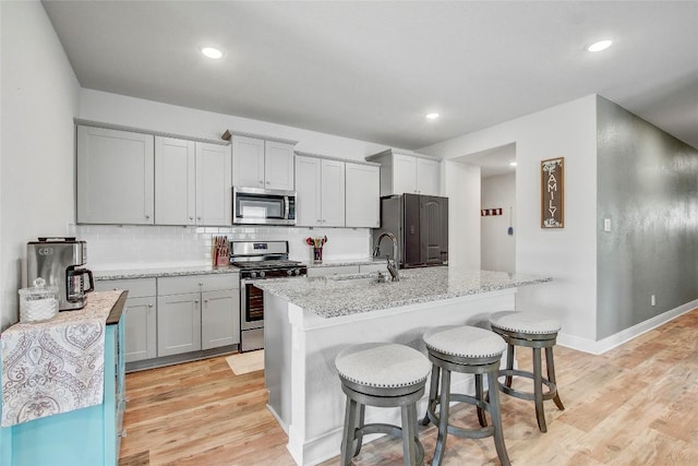 kitchen featuring a kitchen bar, light stone countertops, a center island with sink, and stainless steel appliances