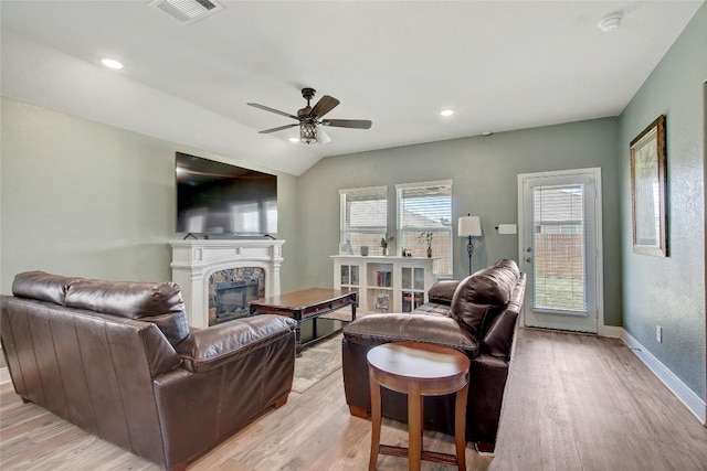 living room with a stone fireplace, ceiling fan, light hardwood / wood-style flooring, and vaulted ceiling