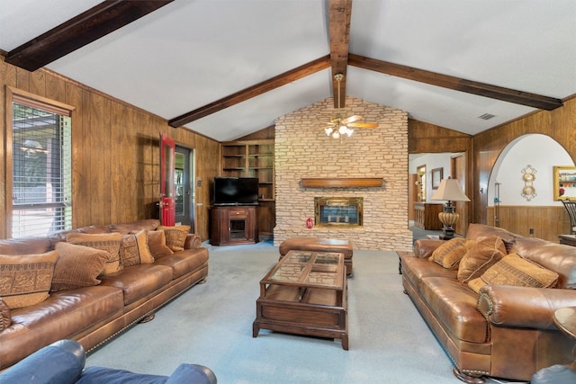 living room with ceiling fan, wood walls, a fireplace, lofted ceiling with beams, and light colored carpet