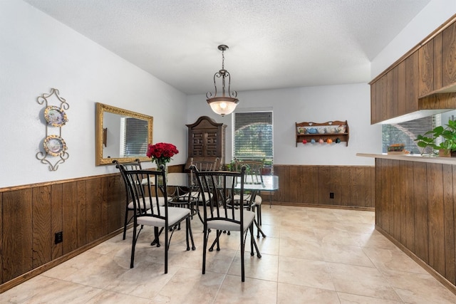 dining space with light tile patterned flooring, a textured ceiling, and wooden walls