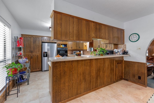 kitchen featuring black double oven, kitchen peninsula, a textured ceiling, and stainless steel refrigerator with ice dispenser