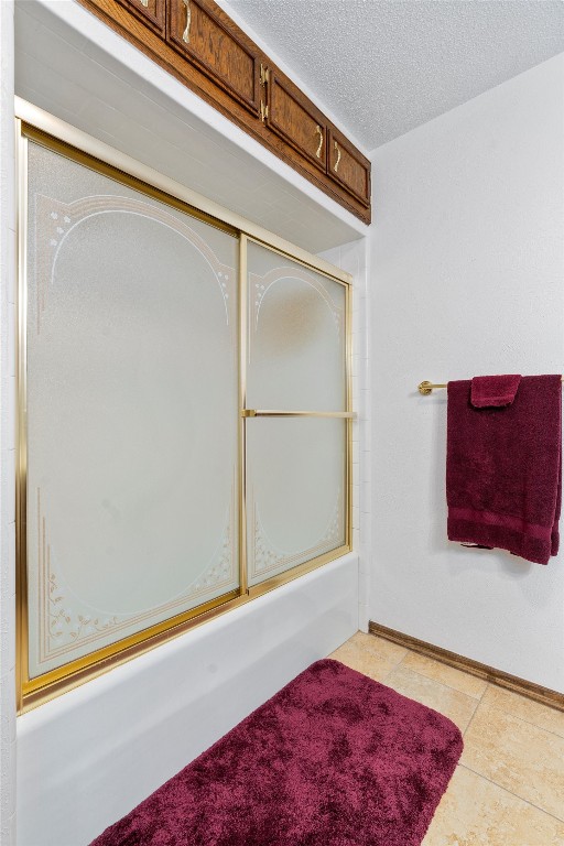 bathroom with combined bath / shower with glass door, a textured ceiling, and tile patterned flooring