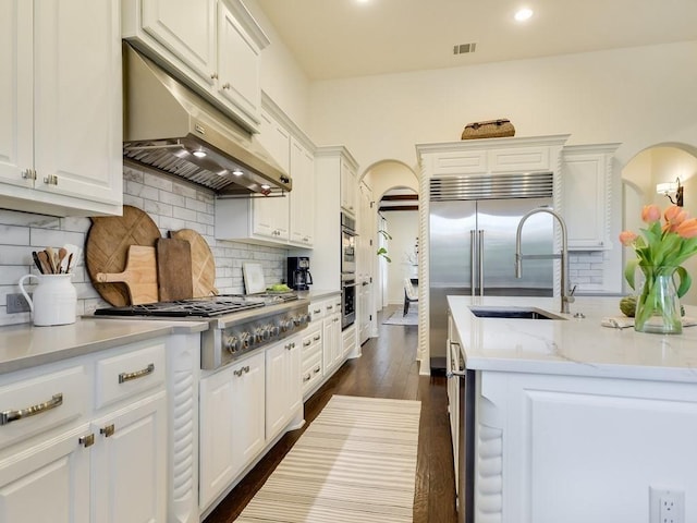 kitchen featuring dark wood-type flooring, stainless steel appliances, tasteful backsplash, light stone counters, and white cabinets