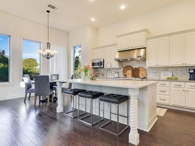 kitchen featuring sink, appliances with stainless steel finishes, dark hardwood / wood-style floors, pendant lighting, and a kitchen island with sink